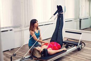 Woman exercising on Pilates reformer with personal trainer.